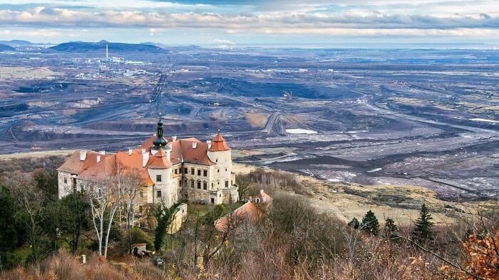Abandoned castle overlooking a vast, barren landscape with mining scars, resembling a dystopian nightmare scene.