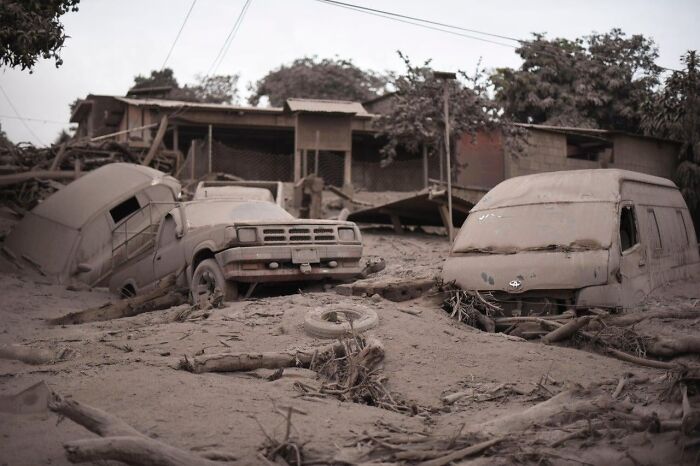 Abandoned vehicles covered in ash and debris in a desolate area resembling a dystopian nightmare scene.