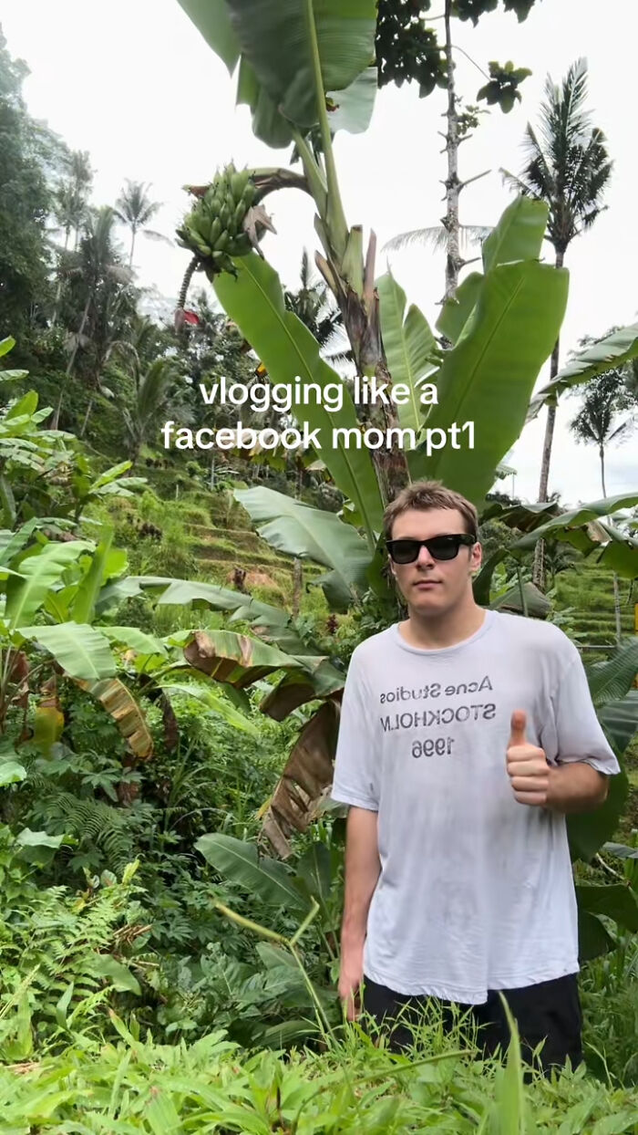 Young man wearing sunglasses and a white shirt posing with thumbs up in lush greenery, capturing chaotic energy of mom selfies.