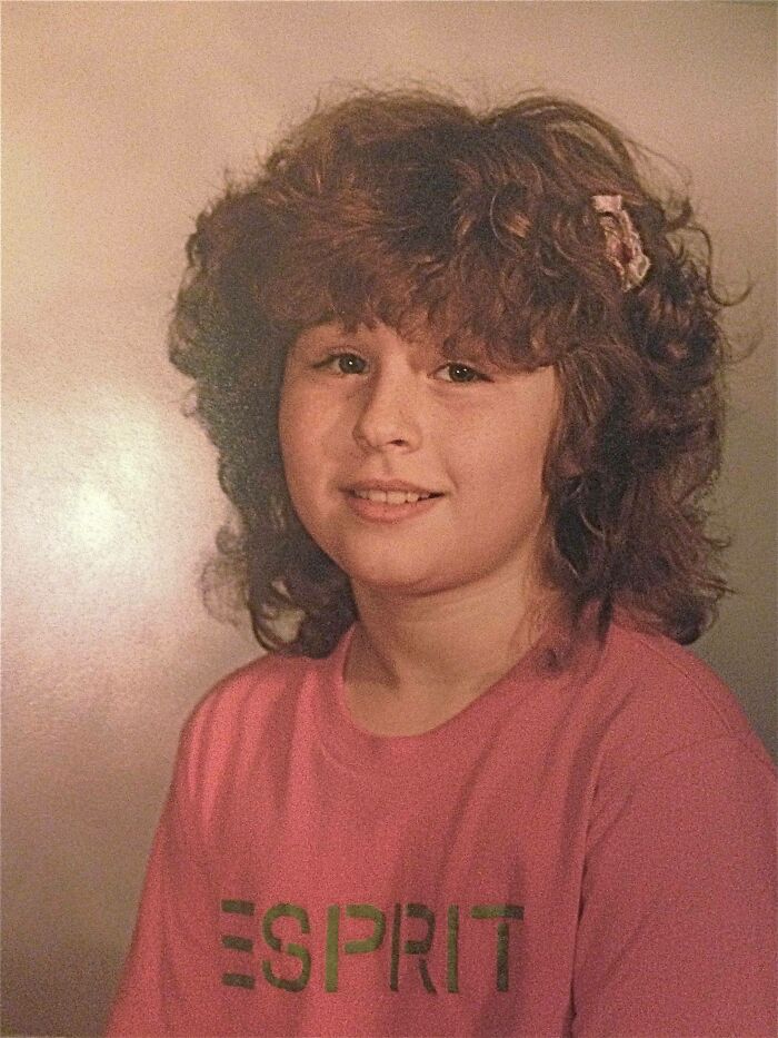 Young girl with iconic 80s hairdo featuring voluminous curly layers and a hair clip, wearing a pink Esprit shirt.