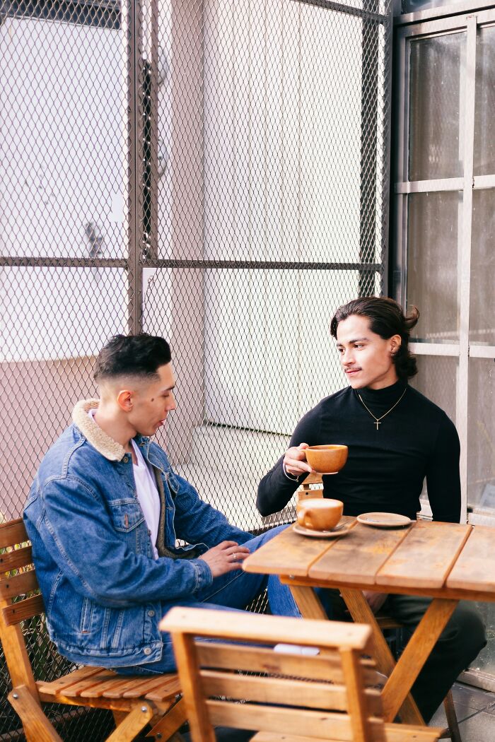 Two men sitting at a wooden table having coffee, showing potential red flags during a first date conversation.
