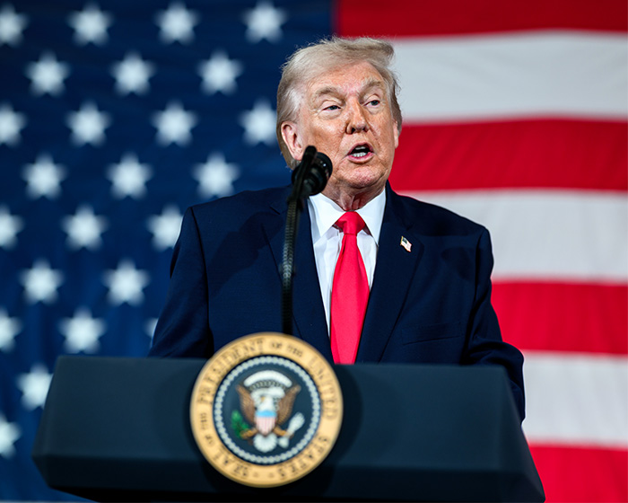 Former President Trump speaking at a podium with presidential seal, American flag in background, discussing UFO files release.