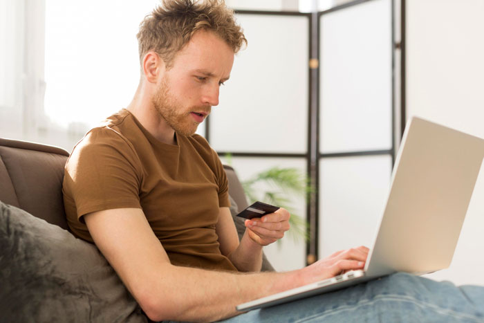 Man using laptop and holding credit card, focused on turning bike spare parts into a profitable payday online.