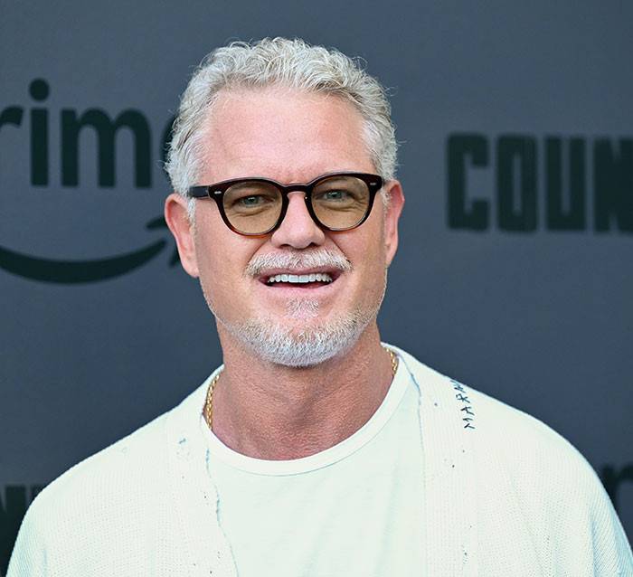Eric Dane smiling, wearing round glasses and a white shirt at a public event about GoFundMe backlash.