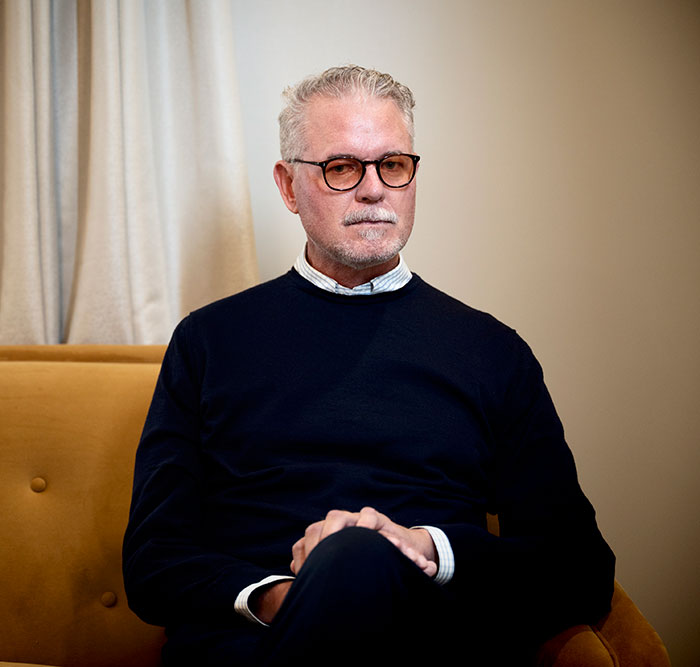Eric Dane seated indoors wearing glasses and a dark sweater, illustrating the first symptom leading to ALS diagnosis.