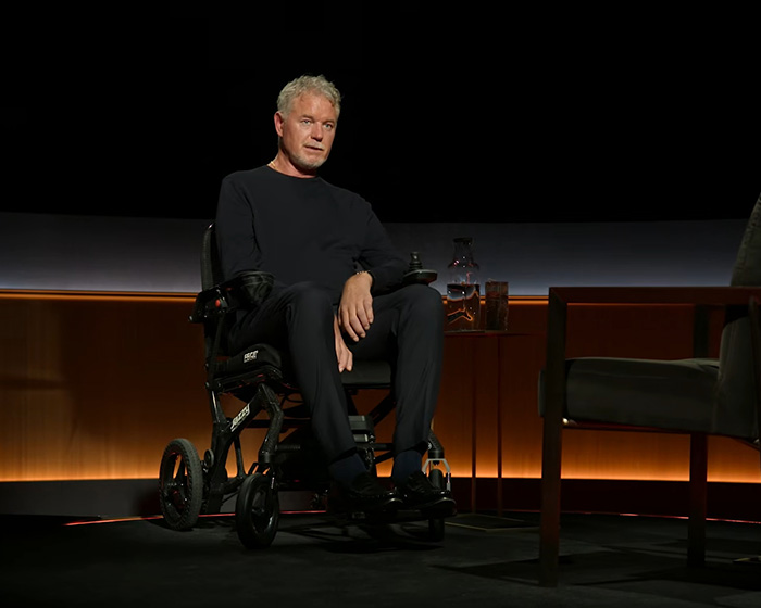 Eric Dane seated in a wheelchair on a dimly lit stage, reflecting the heartbreaking last words for his teenage daughters.