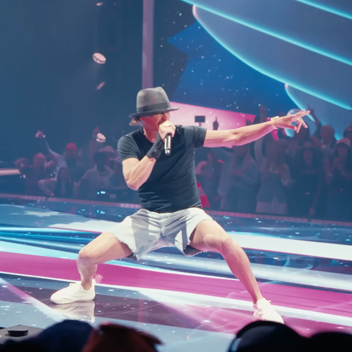 Male performer in a hat and shorts on stage during Turning Point USA's alternate halftime show with an energetic audience.