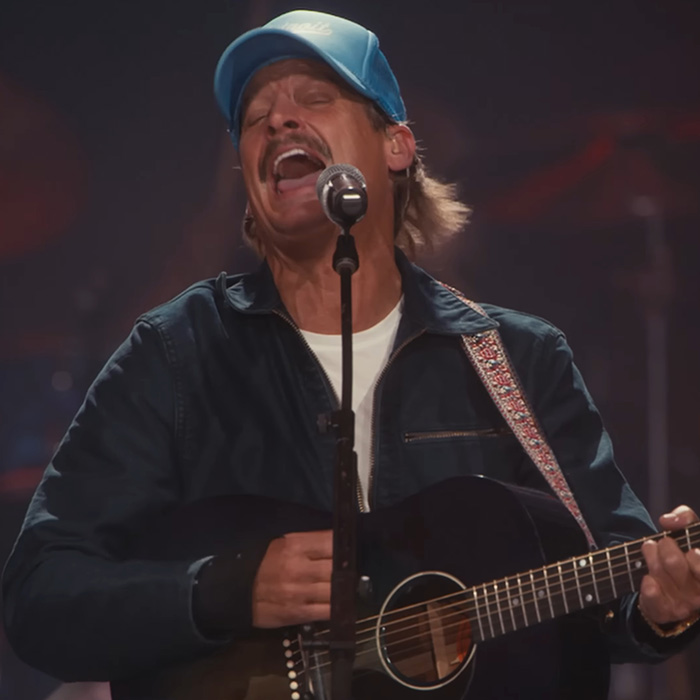Male musician passionately singing and playing guitar during Turning Point USA alternate halftime show performance.