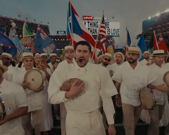 Performers in white outfits with flags and drums at a football stadium during Turning Point USA alternate halftime show.