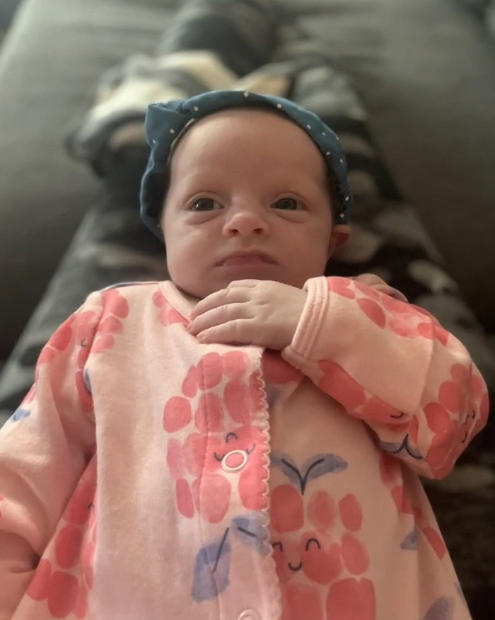 Infant baby girl wearing pink floral outfit and blue headband lying down, related to horrifying exchange between young parents.