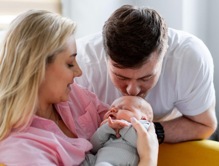 Woman marrying high school bestie for tax perks, sharing tender moment with baby and partner&rsquo;s playful surprise.