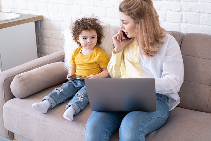Mother distracted on phone while child sits beside her on couch, illustrating family dinner ruin by rude behavior.
