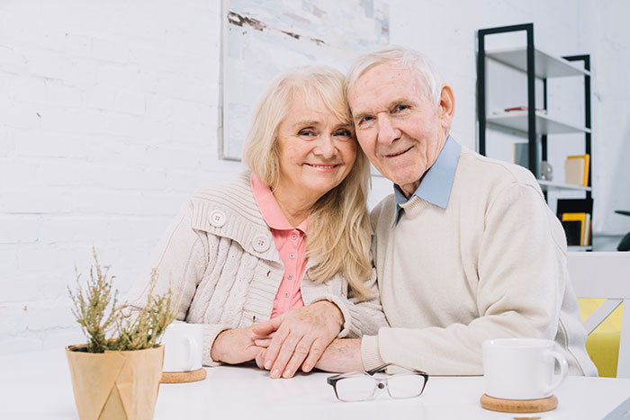 Elderly couple smiling warmly at home, sharing a peaceful moment during a family dinner with a rude mother present.
