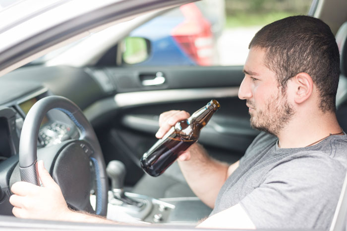 Man holding a beer bottle inside a car, illustrating parents favoritism leading to favored child turning into a criminal.