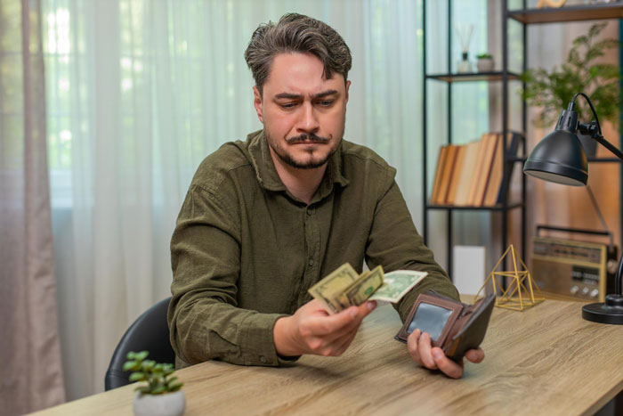 Man with a mustache counting money from a wallet, reflecting on the impact of parents' favoritism and family dynamics.