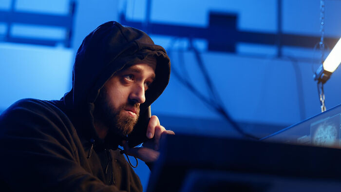 Man in a dark hoodie looking serious while speaking on phone, depicting emotional reality of being related to an ICE agent.