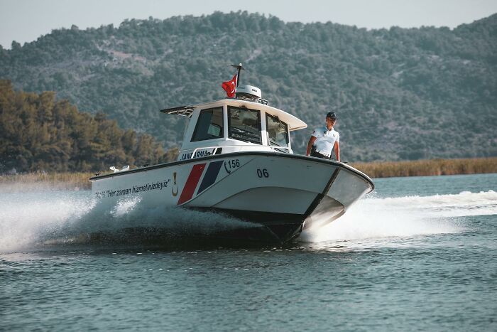 Small patrol boat with officer on bow cruising on water near forested hills, illustrating the emotional reality of being related to an ICE agent.