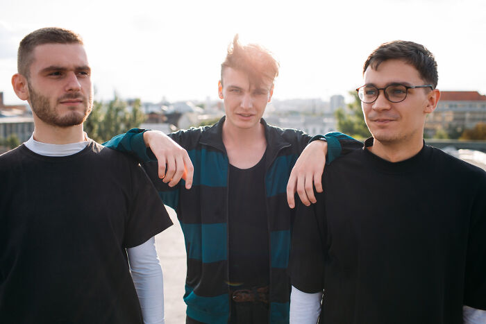 Three young men standing outdoors, showing complex emotions related to being related to an ICE agent.