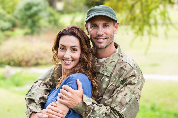 Smiling man in military uniform embracing woman outdoors, representing the emotional reality of being related to an ICE agent.