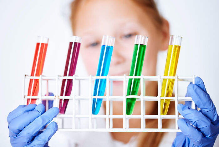 Scientist wearing blue gloves holding test tubes with colorful liquids, symbolizing complex emotions related to ICE agent family ties.