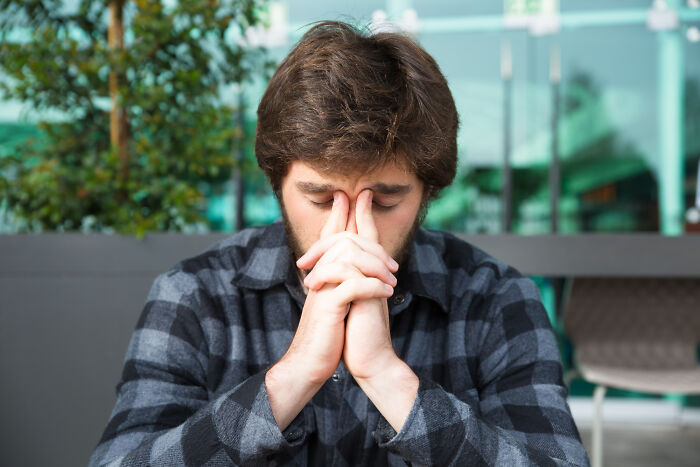 Young man in a checkered shirt showing emotional distress, reflecting on the reality of being related to an ICE agent.