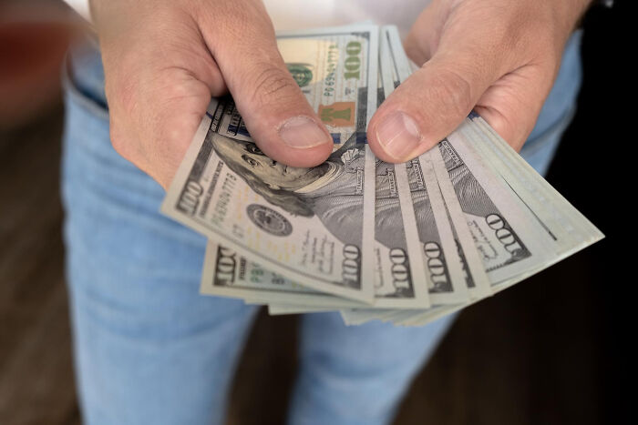 Hands holding multiple 100-dollar bills, illustrating financial aspects related to being connected to an ICE agent.
