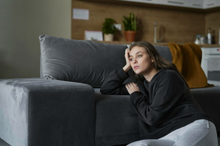 Young woman looking distressed sitting on the floor by a couch, reflecting the stress of a man's insurance hike impact.