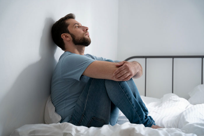 Man sitting on bed looking thoughtful and crushed after overhearing woman confess to bestie about her fianc&eacute; background role.