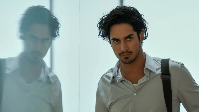 Man with intense expression standing by a glass wall, representing 56 Days ending and book climax changes.