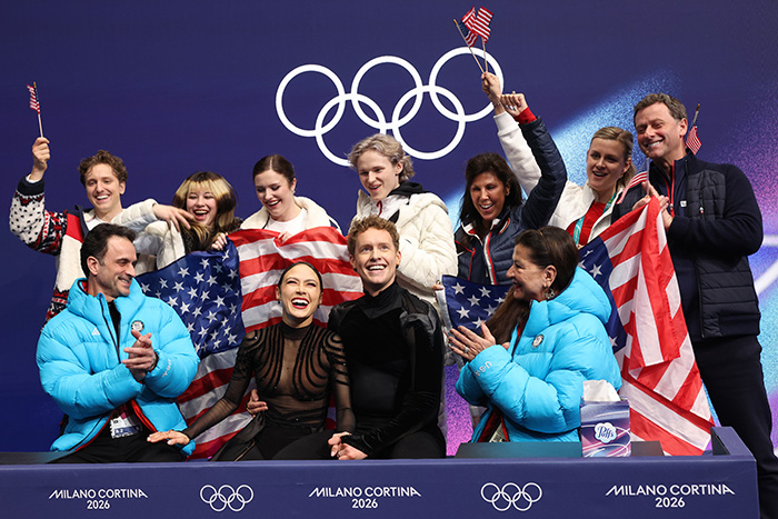 Team USA figure skating athletes and coaches celebrating with American flags at the Olympics amid suspicious scoring claims.