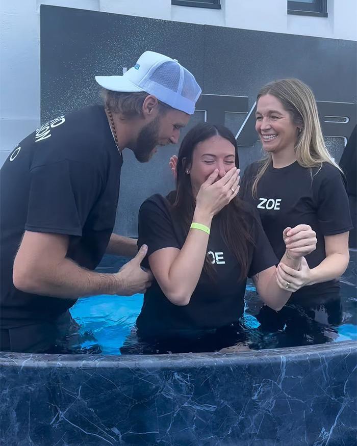 Three people in a baptismal pool smiling and celebrating as former adult star joins Amish community in Pennsylvania.