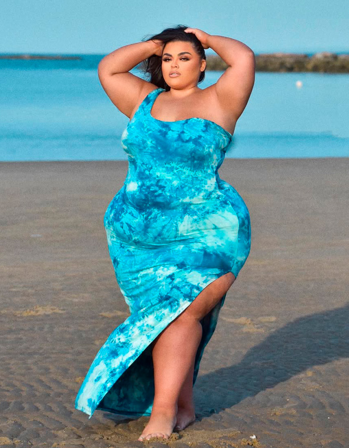 Former body positivity influencer poses confidently in a blue dress on the beach, challenging the radical movement.