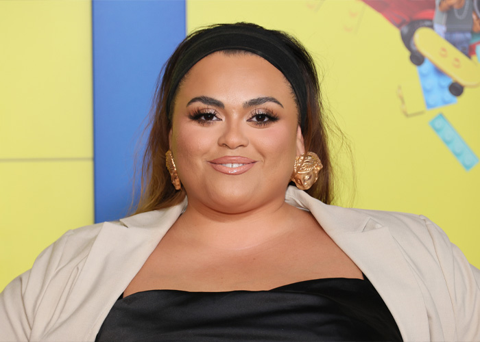Former body positivity influencer with headband and beige blazer posing against a colorful background at an event.