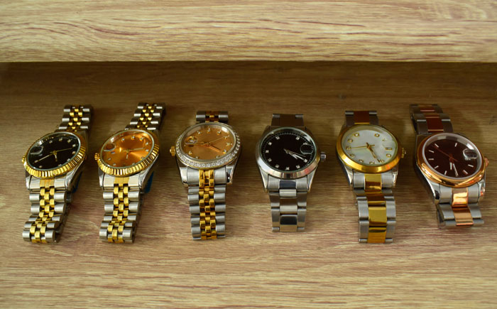 Six luxury watches with metal bands displayed on a wooden surface, highlighting the missing watch in a theft scenario.