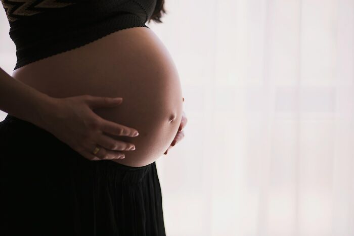 Pregnant woman holding her belly in a dimly lit room symbolizing toxic workplace moments affecting employees.