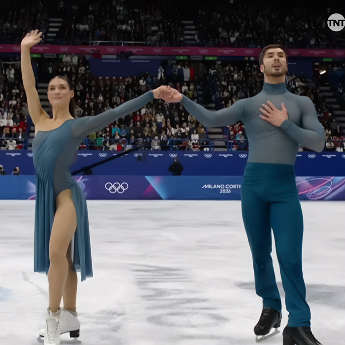 French skater and partner holding hands on ice rink during Olympics amid cheating scandal controversy.