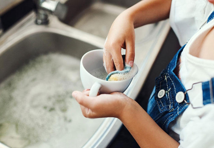 Person washing a delicate teapot by hand in a kitchen sink with soapy water, highlighting care for Yixing teapot. Person washing a delicate teapot by hand in a kitchen sink with soapy water, highlighting care for Yixing teapot.