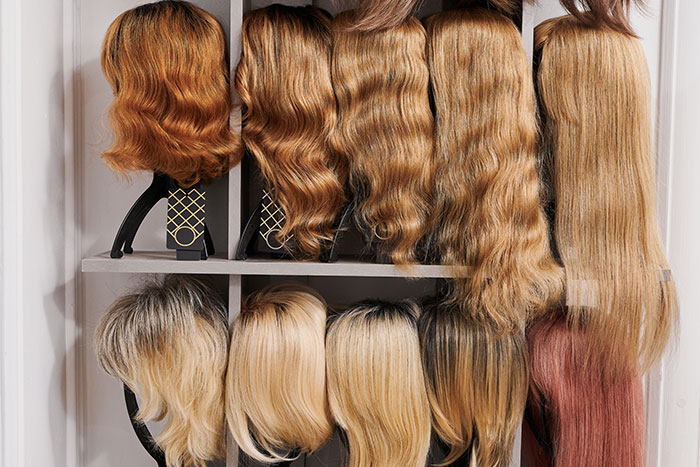 Various long hair wigs displayed on shelves, highlighting textures and colors for sister&rsquo;s wig preparations.