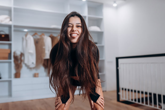 Young woman with long hair leaning forward indoors, showing off her hair amid a casual modern room setting.