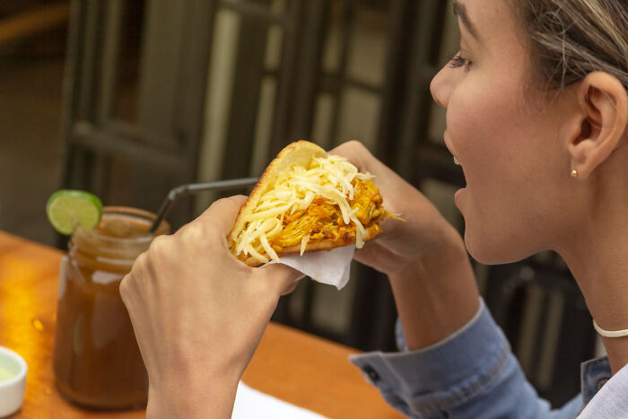 Person holding a sandwich with shredded cheese, with a drink and lime on the table, illustrating hilarious physicians notes humor.
