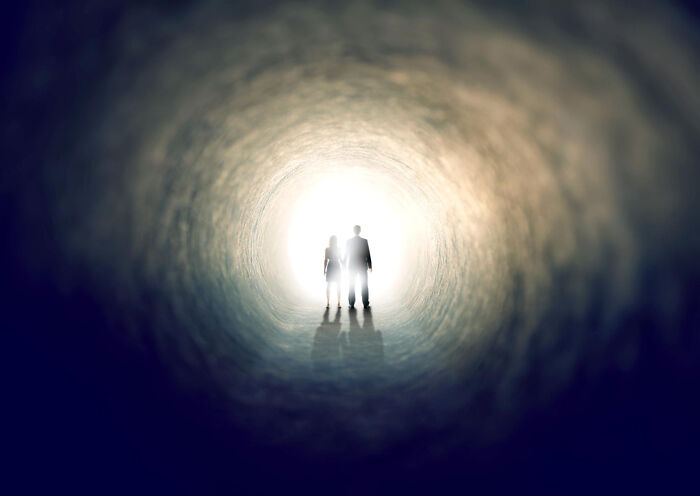 Silhouettes of two people standing at the bright end of a tunnel, symbolizing hope and clarity in physicians' notes.