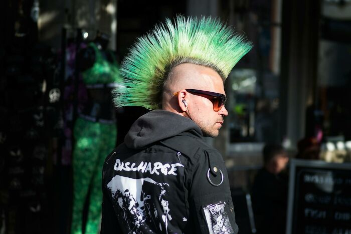 Person with green mohawk and sunglasses wearing a black jacket featuring punk band patches in an urban street setting, humorous physician notes theme.