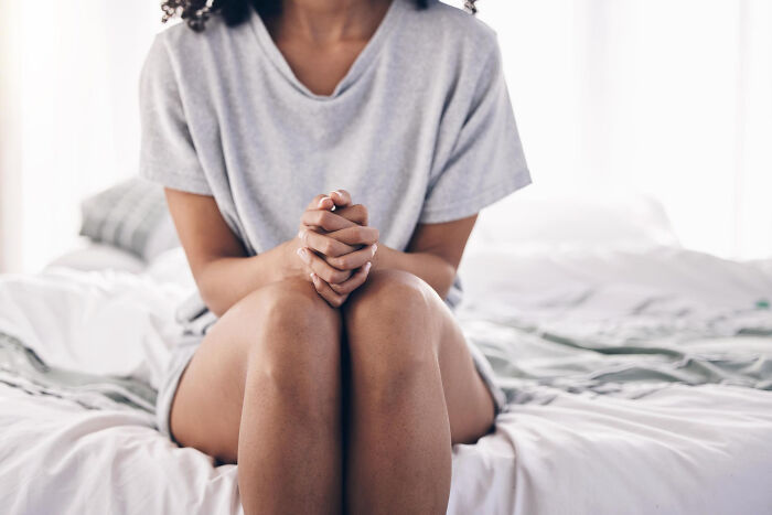 Woman sitting on bed with hands clasped, conveying discomfort related to physicians' notes and medical humor.
