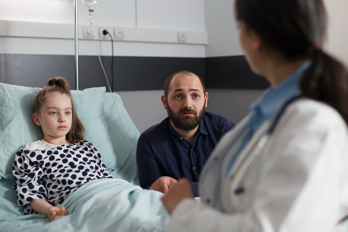 A concerned father and child in a hospital bed listening to a physician discussing hilarious physicians notes.