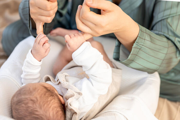 Infant lying down grabbing adult's thumbs, illustrating caring and humorous physicians' notes bringing laughter today.