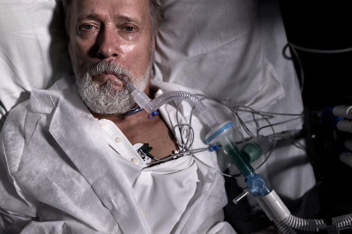 Elderly patient in hospital bed with breathing tube and medical equipment, illustrating physicians' notes and healthcare.