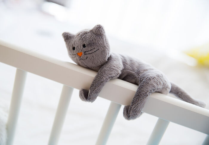 Plush gray cat toy draped over white railing symbolizing a lighthearted and humorous take on physicians notes humor.