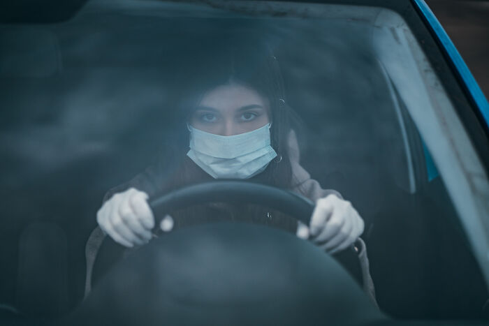 Woman wearing a mask and gloves driving a car, illustrating a concept related to hilarious physicians' notes.