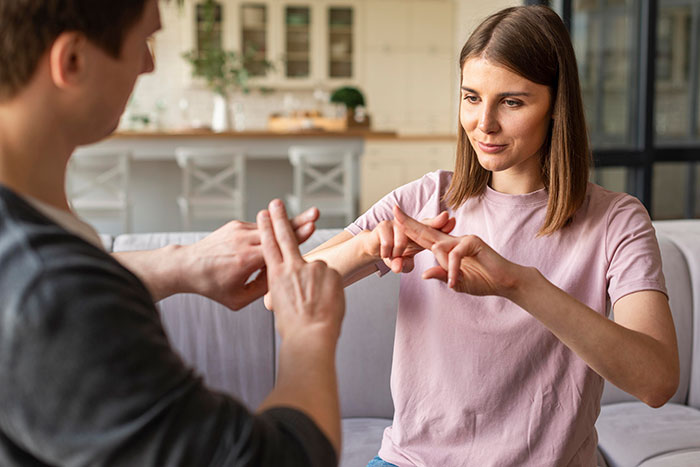 A young woman and man using sign language together in a cozy home setting, illustrating communication under anesthesia.