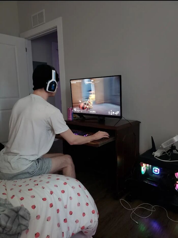 Young man wearing headphones awkwardly sitting while gaming on a computer, illustrating awkward body language for men.
